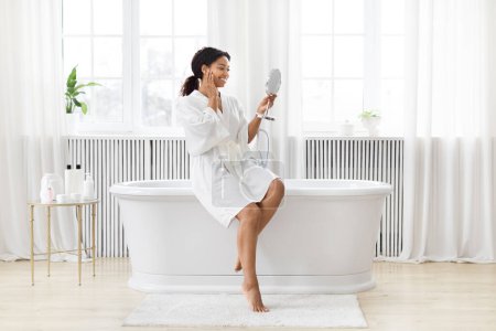 Téléchargez les photos : Dans une salle de bain bien éclairée, la femme afro-américaine s'amuse à chanter dans un miroir de poche, se sentant joyeuse - en image libre de droit
