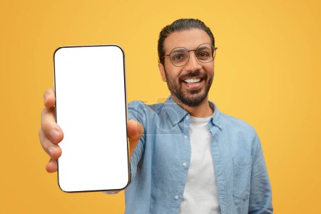 Téléchargez les photos : Homme indien confiant présente un téléphone avec écran blanc vierge, parfait pour l'affichage de conception - en image libre de droit