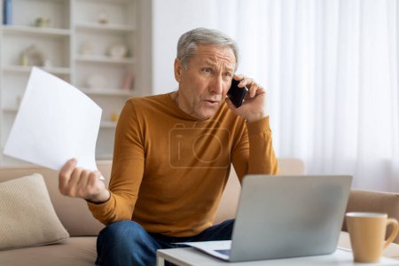Besorgt schauender älterer Mann telefoniert mit Dokumenten, während er einen Laptop benutzt, vielleicht mit Arbeit oder Finanzen