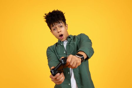 Photo for African american guy shows excitement while holding a game controller against a yellow background - Royalty Free Image