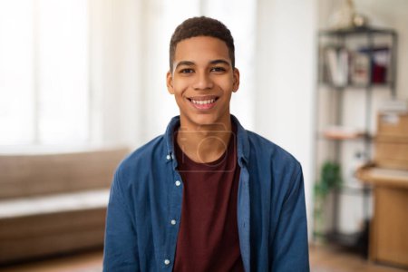 Photo for A cheerful young man in a casual shirt and jacket poses with a bright smile in a cozy home environment - Royalty Free Image