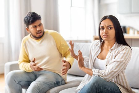 Un joven indio hombre y mujer están teniendo una discusión acalorada mientras están sentados en un sofá.