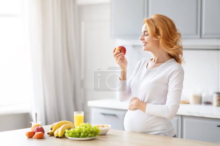 Mujer embarazada saludable en una cocina ordenada seleccionando una fruta entre varias opciones saludables