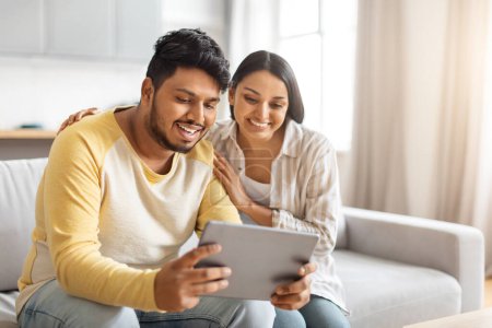Photo for Indian man and a woman are seated on a couch, both engrossed in tablet device. They are focused and engaged with the screen. - Royalty Free Image