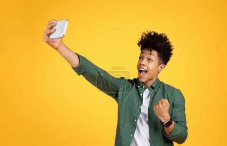 Energetischer schwarzer Kerl macht eine Faustpumpe, während er ein Selfie auf leuchtend gelbem Hintergrund macht