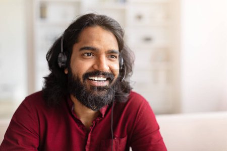 Happy Indian man wearing headphones and smiling broadly in front of laptop screen, closeup, copy space