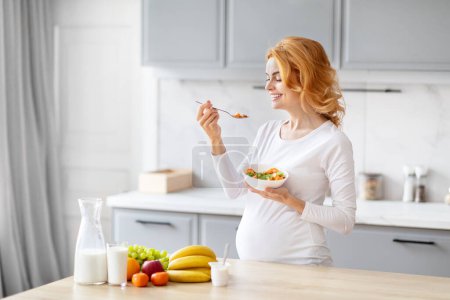 Photo for A pregnant woman in a modern kitchen setting eating a bowl of salad, embodying health and nutrition during pregnancy - Royalty Free Image