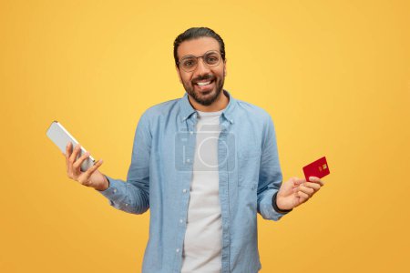 Homme indien souriant tenant un smartphone et une carte de crédit, idéal pour les concepts de shopping en ligne