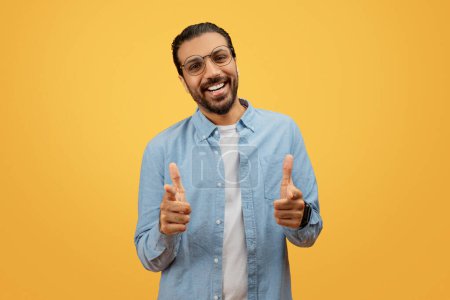 Cheerful bearded indian man with glasses giving double thumbs up on a yellow background