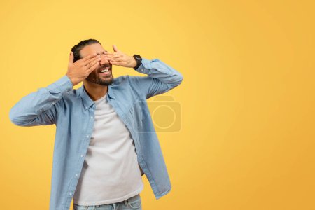 Photo for Eastern guy in a casual outfit with their face blurred out expressing shock or disbelief, set against a vibrant yellow background - Royalty Free Image