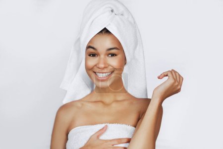 Téléchargez les photos : Fille afro-américaine souriante avec épaules nues et serviette sur la tête dans le spa. Bonne journée spa concept - en image libre de droit