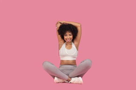 Foto de Una mujer afroamericana feliz en una pose de yoga con las manos apretadas por encima de su cabeza sobre un fondo rosa - Imagen libre de derechos