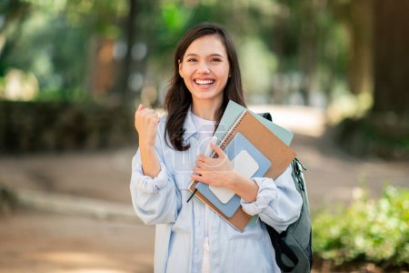 Photo for A joyful pretty young woman student celebrates with a fist pump in an outdoor park setting, pass exam - Royalty Free Image