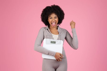 Photo for Cheerful african american woman holding a scale, celebrating progress in her weight loss journey - Royalty Free Image