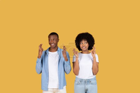 Foto de Hombre y mujer afroamericanos cruzan los dedos con esperanza o piden un deseo sobre un fondo amarillo - Imagen libre de derechos