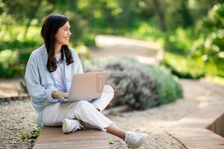 Photo for A woman works on a laptop, sitting comfortably outdoors, showcasing flexibility of remote work, copy space - Royalty Free Image
