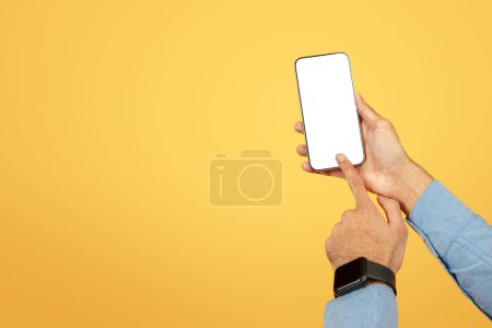 Téléchargez les photos : Une main présentant un smartphone avec un écran vierge et modifiable sur un fond jaune chaud pour les maquettes - en image libre de droit