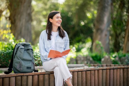 Photo for Tranquil scene of a young woman student engrossed in a book, sitting on a park bench, looking ay copy space - Royalty Free Image
