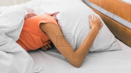 Foto de Falta de sueño. Mujer cubriendo la cabeza con almohada, despertando por la mañana - Imagen libre de derechos