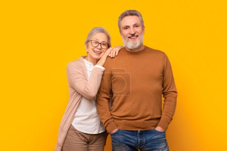 Téléchargez les photos : Heureux couple âgé caucasien embrasse dans un studio jaune toile de fond, rayonnant d'amour et de chaleur du mariage à long terme. Concept d'affection mature et de compagnie durable - en image libre de droit