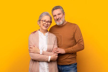 Téléchargez les photos : Prise de vue en studio d'un heureux couple de personnes âgées en tenue décontractée posant ensemble sur fond de studio jaune. Portrait de conjoints souriant à la caméra et étreignant. Concept de mariage heureux - en image libre de droit