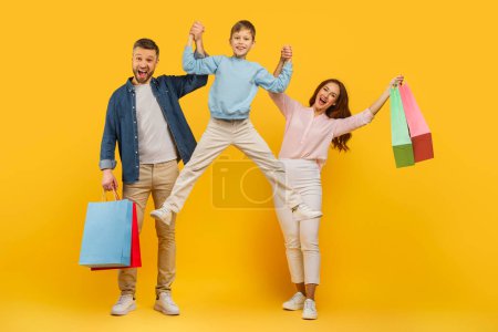 An energetic and joyful family with shopping bags jumping and celebrating on a vivid yellow background