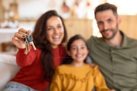 Eine glückliche dreiköpfige Familie mit der Mutter, die einen Satz Hausschlüssel hochhält, was darauf hindeutet, dass sie gerade ein neues Haus gekauft haben