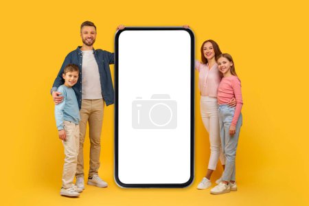 Happy family presenting big smartphone screen mockup copy space for mobile app advertisement, isolated on yellow