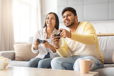 Photo for Indian man and woman are seated on a couch, immersed in playing a video game together. - Royalty Free Image