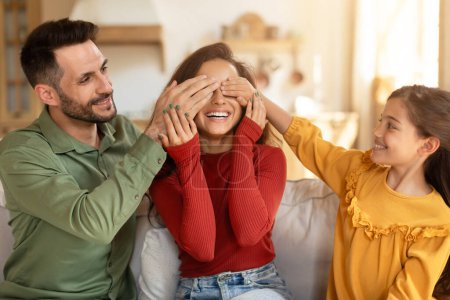 Photo for A family enjoys a playful moment with the daughter participating in a joyful surprise for her mother, full of laughter - Royalty Free Image