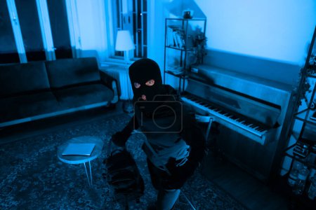 Masked burglar with a backpack inspects a living room environment, planning their next move carefully