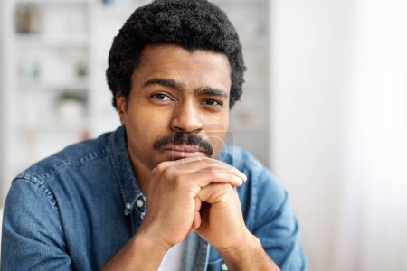Un primer plano de un hombre negro pensativo apoyando su barbilla en su mano, mirando ligeramente fuera de cámara.