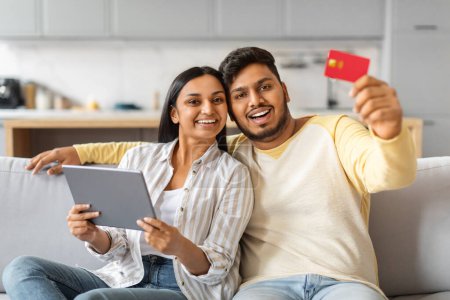 Foto de Hombre y mujer indios están sentados en un sofá, sosteniendo una tableta y una tarjeta de crédito en sus manos. - Imagen libre de derechos