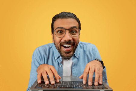Téléchargez les photos : Homme indien joyeux utilisant un ordinateur portable avec une expression enthousiaste, idéal pour les thèmes technologiques - en image libre de droit