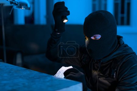 Ein gezielter Einbrecher benutzt eine Taschenlampe, um in einem dunklen Raum Geld zu stehlen, möglicherweise auf der Suche nach persönlichen Informationen