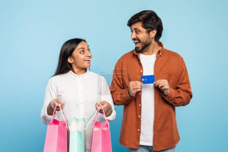 Téléchargez les photos : Homme et femme indiens tiennent joyeusement des sacs à provisions et une carte de crédit, symbolisant le consumérisme et les loisirs - en image libre de droit