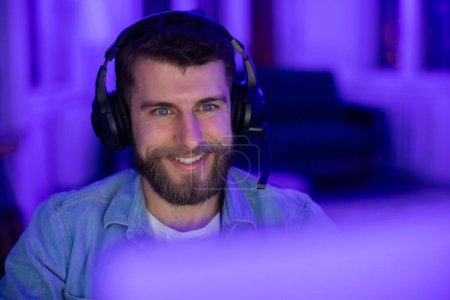 Contented man gamer with a smile playing games at night with vibrant purple background lighting, closeup