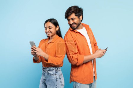 Casual jeune couple indien en utilisant leurs téléphones, absorbé dans les mondes numériques personnels avec toile de fond bleue
