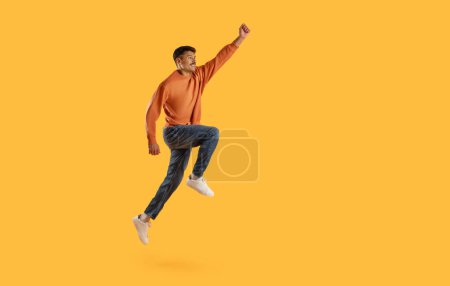 Captivating man in mid-air jump with fist triumphantly raised, against a bright yellow background, exuding joy and energy