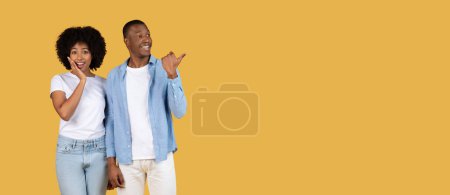 Photo for African American man and woman, happily wave and smile, standing close on a yellow backdrop, copy space - Royalty Free Image