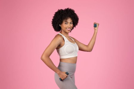 Smiling african american woman in sportswear showing her bicep, demonstrates strength and happiness while working out