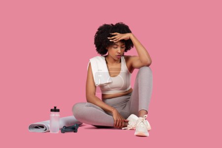 Photo for Exhausted african american lady athlete taking a break and wiping sweat, showing the effort of a workout - Royalty Free Image