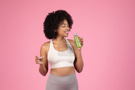 Téléchargez les photos : Femme noire sportive savoure un goût de jus vert, les yeux fermés dans le plaisir - en image libre de droit