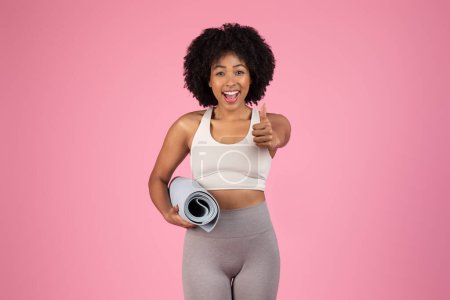 Photo for Cheerful african american woman carrying yoga mat showing thumbs up - Royalty Free Image