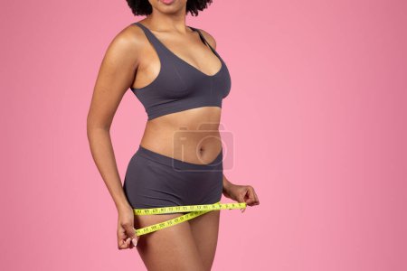 Fit junge afrikanisch-amerikanische Frau misst ihre Taille mit einem Klebeband, das Gesundheits-, Wellness- und Fitnessziele anzeigt