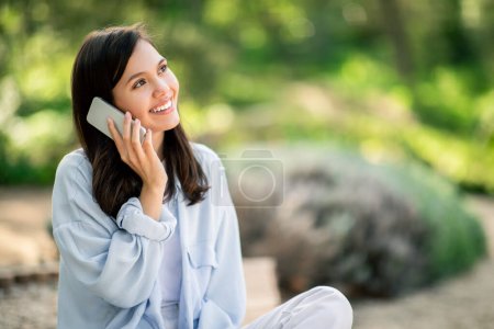 Téléchargez les photos : Une jeune femme joyeuse discute sur son téléphone portable au milieu d'un jardin luxuriant, illustrant la connectivité moderne - en image libre de droit