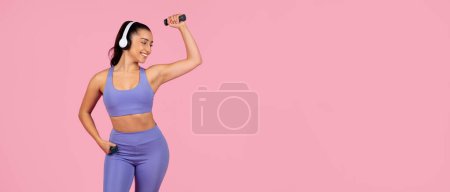 Foto de Una mujer en forma en un sujetador deportivo y polainas escucha música, baila y se divierte sobre un fondo rosa - Imagen libre de derechos