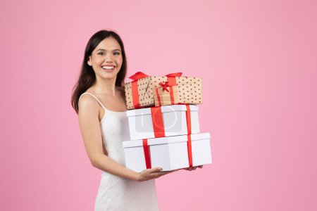 Foto de Una mujer alegre en un vestido blanco sostiene una variedad de cajas envueltas con cintas, expresando felicidad y generosidad - Imagen libre de derechos