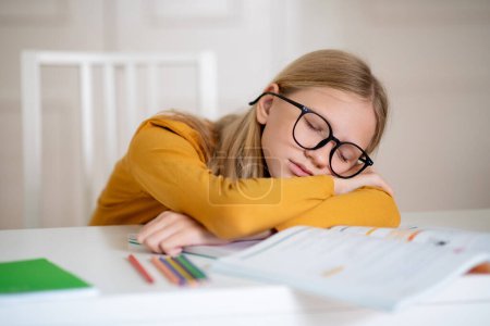 Une jeune fille est assise à une table, absorbée par la lecture d'un livre.