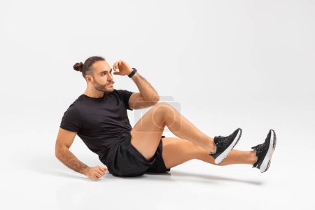 Fit man engages in sit-ups, demonstrating core strength and dedication to fitness on white studio background